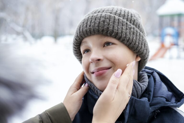 Mother applying cream to son face on winter day